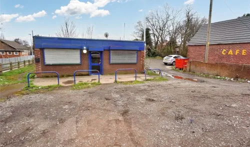 Small commercial building with blue facade and shutters, gravel parking area, and adjacent cafe building.