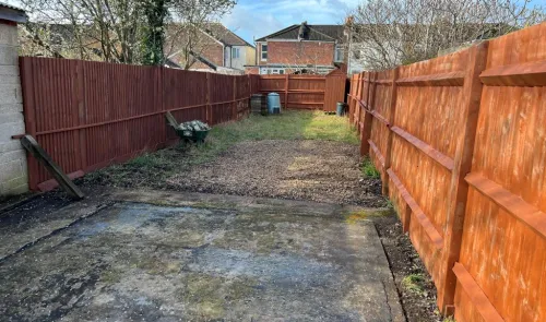 Long, narrow backyard with wooden fences, concrete pad, and small grassy area.