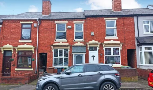 Red brick terraced house exterior with white window frames and parked car.