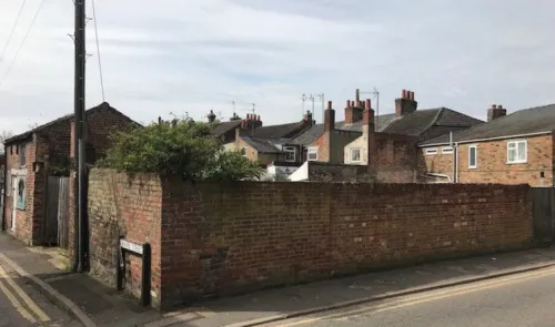 Brick wall and backs of terraced houses seen from a residential street corner.