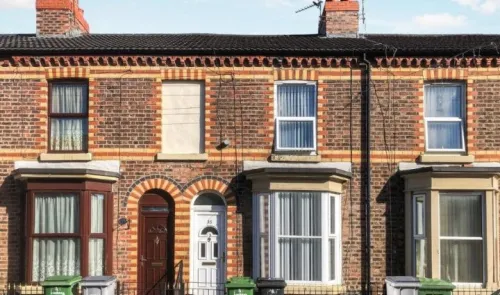 Red brick terraced houses with bay windows, white doors and wheelie bins.
