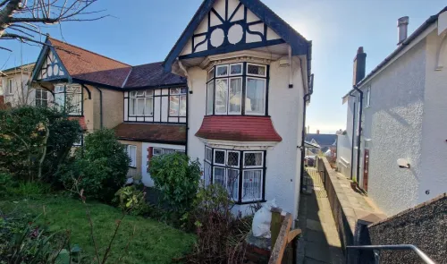 White detached house with mock Tudor features, bay windows, front garden, and a side path.