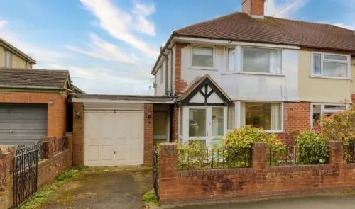 Suburban semi-detached house with attached garage, front garden, and brick wall.