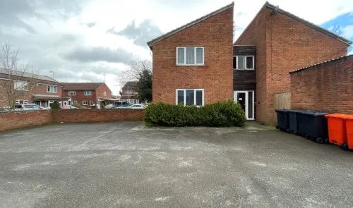 Red brick duplex with a large paved front area and some bins. Other terraced houses are visible in the background.