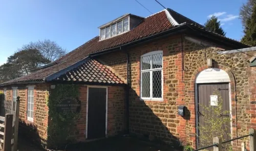 Brick and stone building with tiled roof, multiple windows, and "Kingdom Hall of Jehovah's Witnesses" sign.