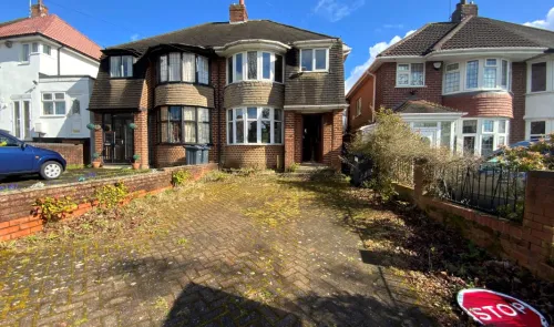 Brick semi-detached house with bay windows and overgrown front driveway. A discarded "STOP" sign lies on the ground.