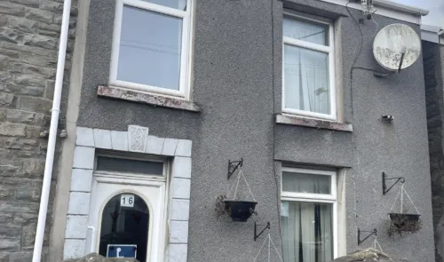 Gray terraced house exterior with white trim, hanging planters, and visible house number 16.