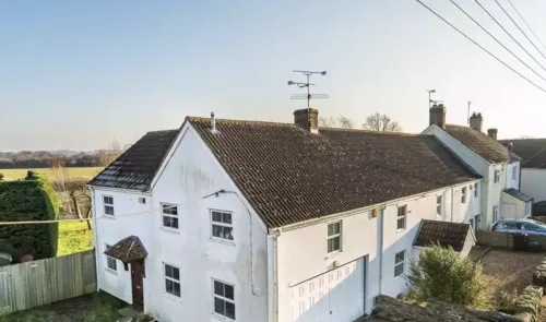 White detached house with tiled roof, attached garage, and green yard. Rural setting.