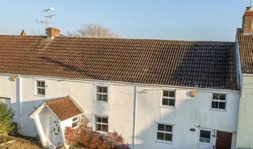 White detached house with brown tiled roof and quirky angled porch.