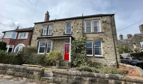 Stone house with red door, white-framed windows, and a low stone wall.