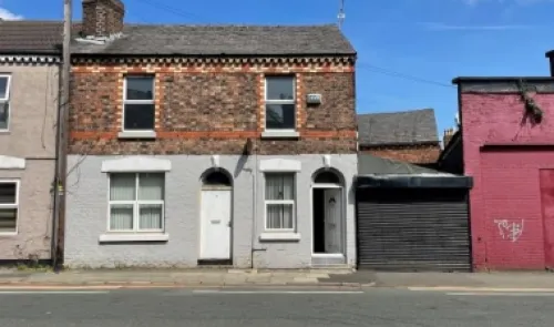 Brick terraced house with partially painted facade, open front door, and attached garage.