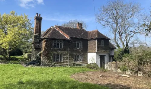 Two-story weathered timber house with brick chimneys on a green lawn.