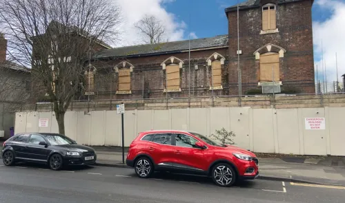Boarded-up brick building behind a construction hoarding. "Dangerous Building. Do Not Enter" sign visible.