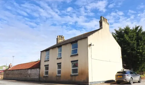 Cream-colored two-story house with multiple windows and chimneys, viewed from the street corner.