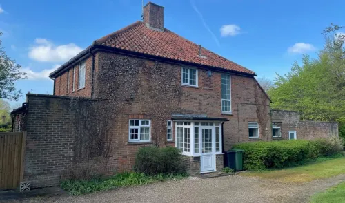 Red brick house with white porch and climbing ivy, under a blue sky.