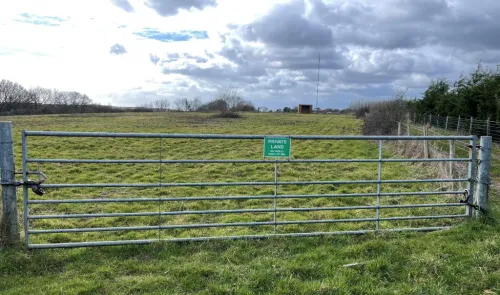 Metal gate across grassy field; "Private Land" sign visible.