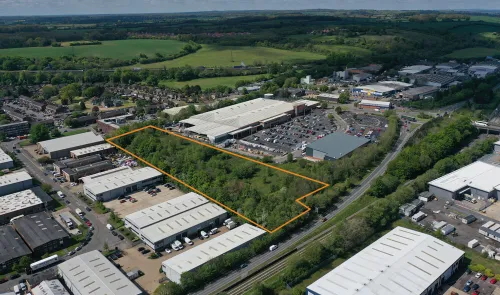 Aerial view of commercial land for sale, outlined in orange, surrounded by industrial units and retail parks.