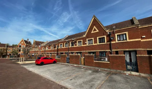 Red car parked in front of a row of modern brick townhouses under a blue sky.
