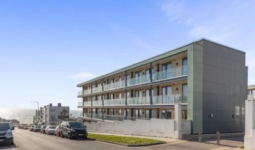 Modern apartment building with glass balconies, ocean view, street parking.