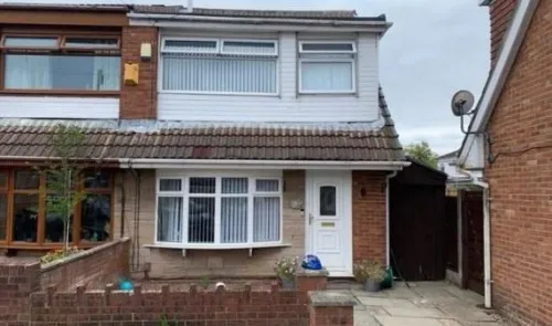 White semi-detached house with bay window and tiled roof. Brick and siding exterior. Small front garden.