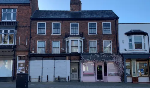 Brick building with white-trimmed windows and a bay window, situated between other commercial properties.