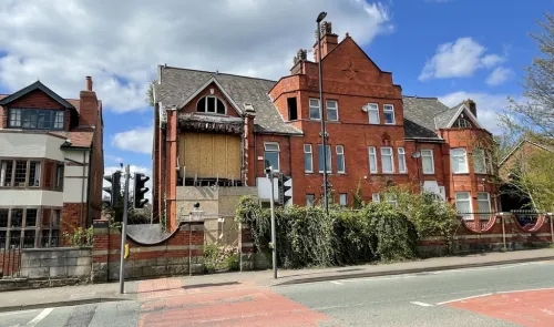 Red brick building with boarded-up section, overgrown ivy, and traffic lights.