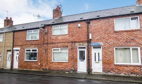 Red brick terraced house with white windows and doors, viewed from across the street.