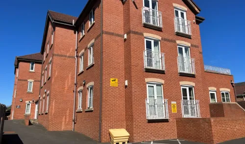 Modern red brick apartment building with white balconies under a clear blue sky.