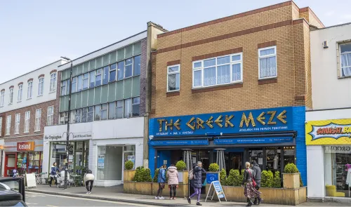 The Greek Meze" restaurant exterior with people outside, plus adjacent shops to let.