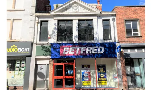 Betfred storefront with red doors, large signage, and promotional posters in a commercial building.