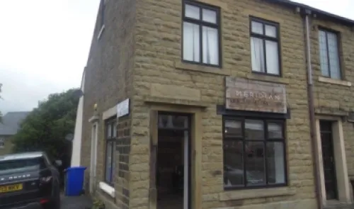 Stone commercial building with "Meridian" sign, black-framed windows, and open front door.