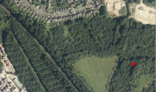 Aerial view of green field, trees, housing, and a quarry.