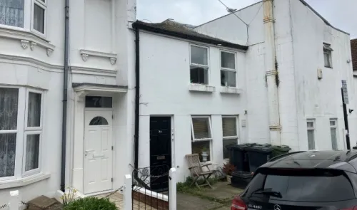 White terraced house exterior with black front door, visible house number and bins.