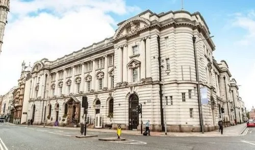 Grand white ornate building with columns on a city street corner.