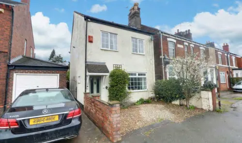 White two-story house with green front door, gravel driveway, and attached garage.