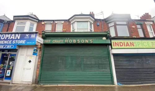 Art Craft Hobson's" storefront with green shutters between other shops on a brick street.