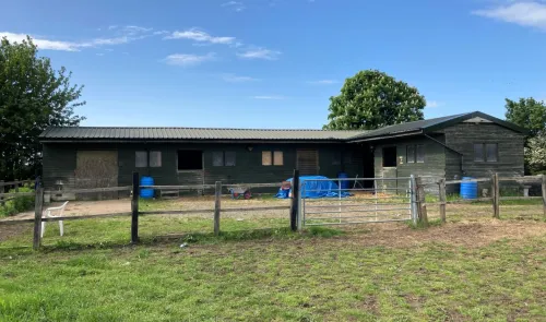 Green stable building with fenced paddock, blue tarp, and wheelbarrow.