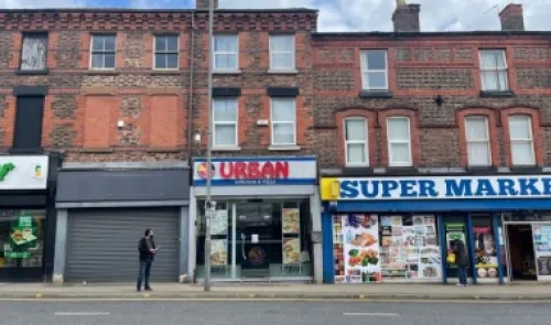 Brick storefronts with "Urban" eatery and supermarket on a city street.