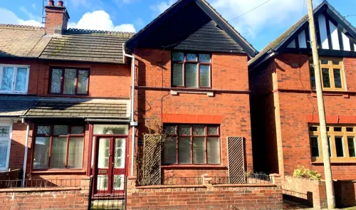 Red brick semi-detached house with dark wood gables and burgundy door and window frames.
