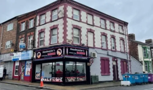 Headmaster's Barber" shop on a street corner, with red and white upper floors.