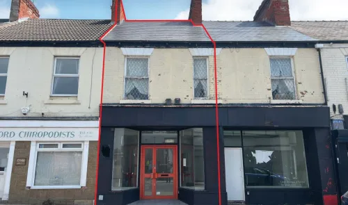Retail property with black storefront and orange double doors, two upper-level windows, and slate roof.