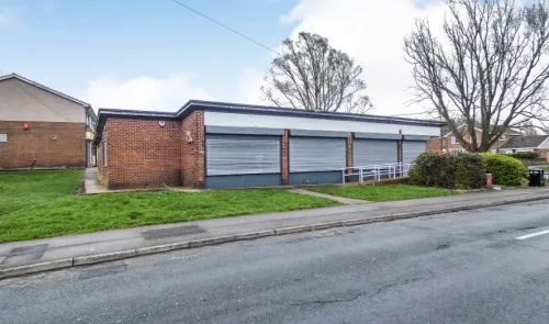 Brick retail building with metal security shutters, ramp access, and roadside parking.