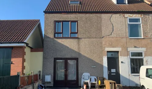 Two-story terraced house exterior with brown roof, pebbledash and brick walls, and brown doors and windows. Some exterior rep