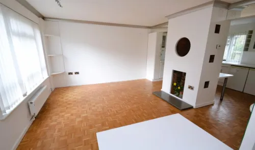 Bright living room with parquet flooring, white walls, built-in shelves, and a unique circular fireplace feature.