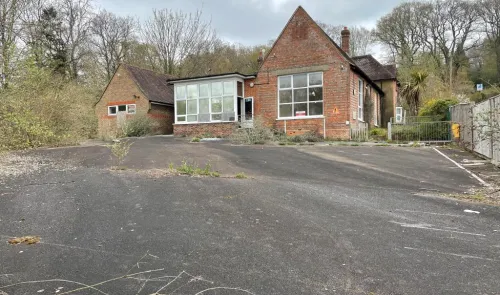 Brick building with conservatory, large paved area, and overgrown foliage.