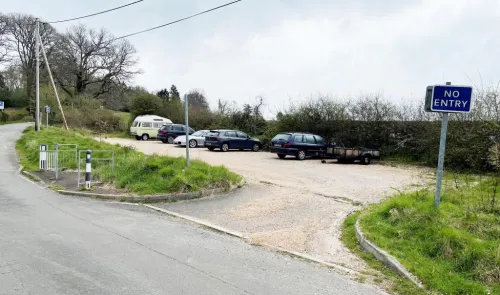 Gravel parking area with cars, campervan, and small trailer. "No Entry" sign visible.
