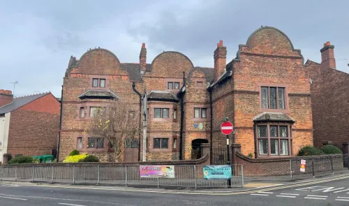 Brick building with curved gables, fenced yard, and "Mersey Open Day" banner.
