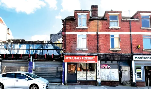 Little Italy Pizzeria" storefront below partially demolished red brick building.