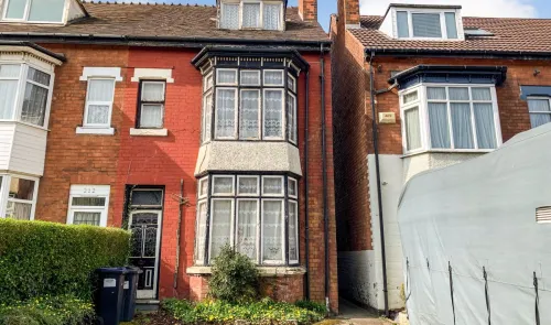 Red brick terraced house with bay windows and lace curtains. Needs renovation.