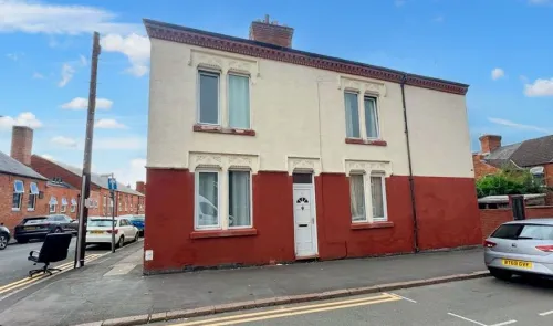 Two-story terraced house with red and cream facade, white front door, and street parking.